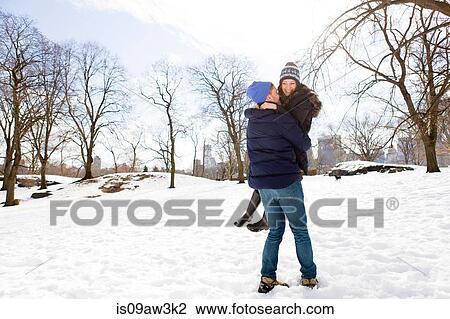 Stock Image - Romantic young man carrying girlfriend in snowy Central Park, New York, USA. Fotosearch