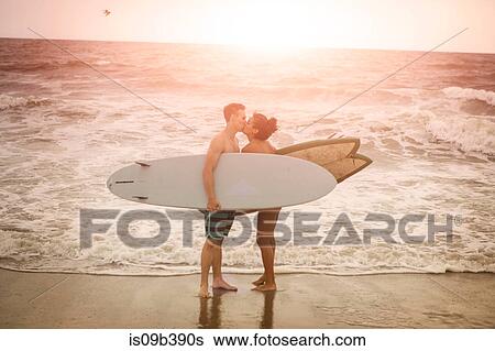 Stock Photograph - Romantic young surfing couple kissing on Rockaway Beach, New York State, USA. Fotosearch