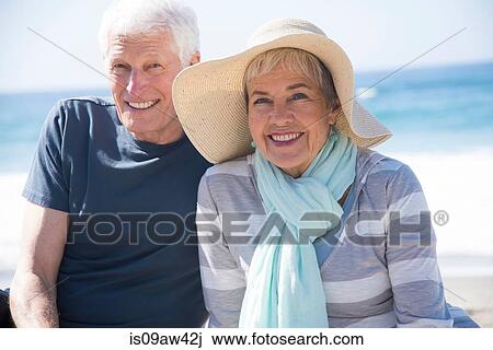 Stock Image - Senior couple relaxing on beach, smiling. Fotosearch