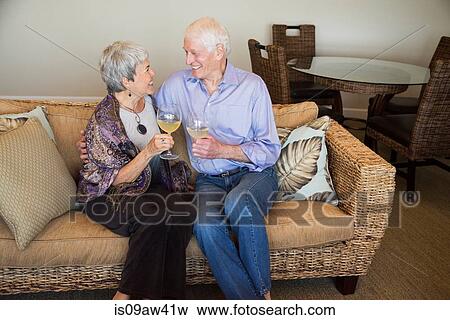 Senior couple relaxing on sofa, holding glass of wine, smiling View Large Photo Image Stock Photo - Senior couple relaxing on sofa, holding glass of wine, smiling. Fotosearch