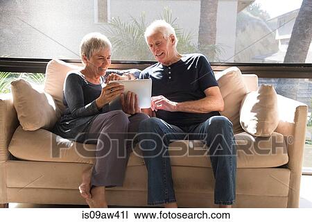 Senior couple, relaxing on sofa, looking at digital tablet View Large Photo Image Stock Image - Senior couple, relaxing on sofa, looking at digital tablet. Fotosearch