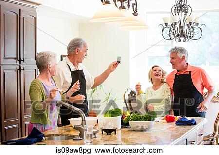 Senior couple taking photograph of friends in kitchen View Large Photo Image Stock Image - Senior couple taking photograph of friends in kitchen. Fotosearch