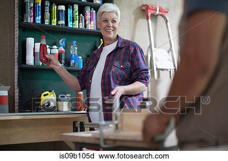Stock Image - Senior female carpenter handing bottle in furniture making workshop. Fotosearch
