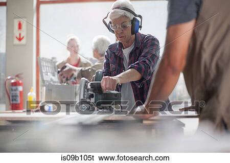 Stock Photograph - Senior female carpenter using power saw in furniture making workshop. Fotosearch