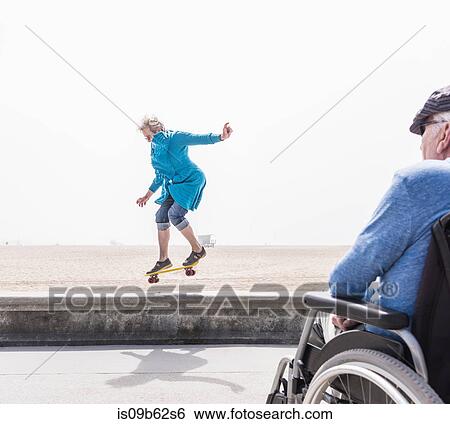 Senior man in wheelchair watching wife doing skateboard trick at beach, Santa Monica, California, USA View Large Photo Image Stock Photograph - Senior man in wheelchair watching wife doing skateboard trick at beach, Santa Monica, California, USA. Fotosearch