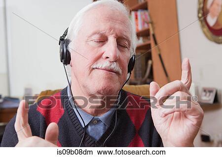Picture - Senior man listening to music on earphones at home. Fotosearch