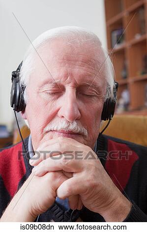 Picture - Senior man listening to music on earphones at home. Fotosearch