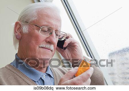 Stock Photography - Senior man reading label on pill bottle at home. Fotosearch