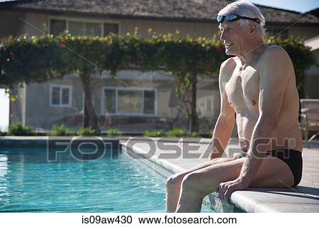 Stock Image - Senior man sitting on edge of outdoor swimming pool. Fotosearch