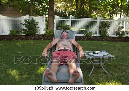 Stock Photo - Senior man sunbathing on garden sun lounger listening to earphones. Fotosearch