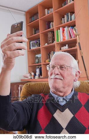 Senior man taking selfie with mobile phone at home View Large Photo Image Stock Image - Senior man taking selfie with mobile phone at home. Fotosearch