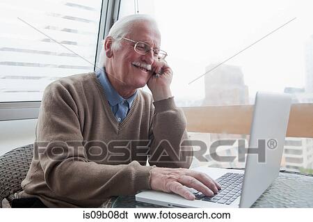 Senior man using mobile phone and laptop at home View Large Photo Image Stock Photograph - Senior man using mobile phone and laptop at home. Fotosearch