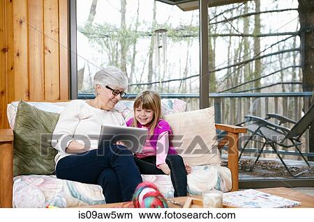 Senior woman and granddaughter browsing digital tablet on living room sofa View Large Photo Image Picture - Senior woman and granddaughter browsing digital tablet on living room sofa. Fotosearch