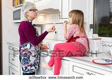 Senior woman and granddaughter eating popcorn at kitchen counter View Large Photo Image Stock Photo - Senior woman and granddaughter eating popcorn at kitchen counter. Fotosearch