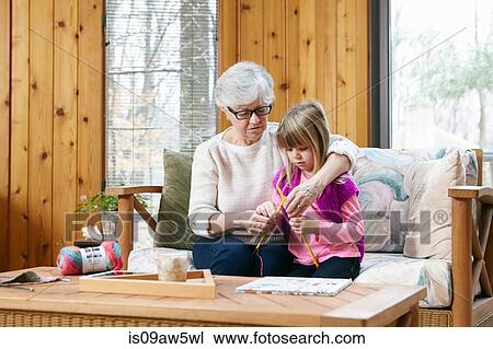 Stock Image - Senior woman and granddaughter knitting together on living room sofa. Fotosearch