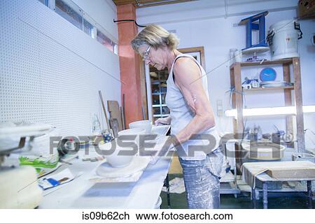 Stock Image - Senior woman in pottery workshop, holding board with three bowls. Fotosearch