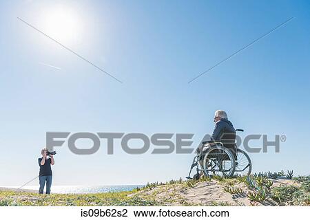 Senior woman photographing husband in wheelchair on dunes, Playa del Ray, California, USA View Large Photo Image Stock Image - Senior woman photographing husband in wheelchair on dunes, Playa del Ray, California, USA. Fotosearch