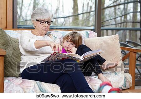 Picture - Senior woman reading story to granddaughter on living room sofa. Fotosearch