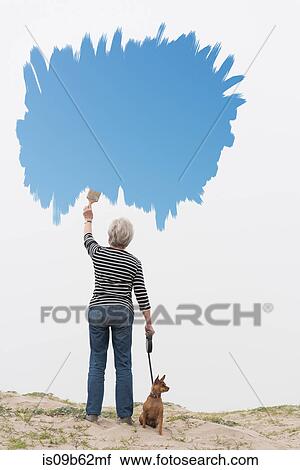 Senior woman with dog on lead painting blue sky in air View Large Photo Image Stock Image - Senior woman with dog on lead painting blue sky in air. Fotosearch