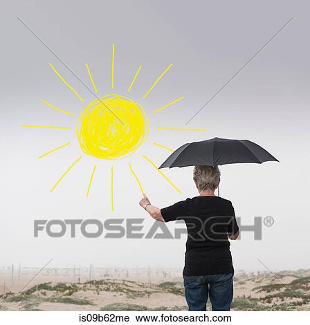 Stock Image - Senior woman with umbrella drawing sun in air. Fotosearch