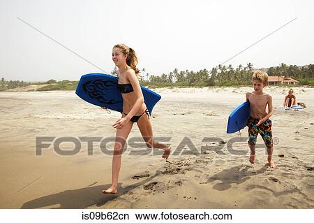Siblings with bodyboards running on beach, Goa, India, Asia View Large Photo Image Picture - Siblings with bodyboards running on beach, Goa, India, Asia. Fotosearch