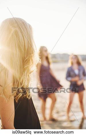 Stock Photography - Side view of blonde woman on beach looking away at friends. Fotosearch