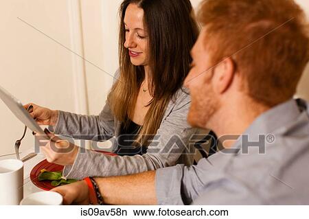 Side view of couple at dining table using digital tablet smiling View Large Photo Image Picture - Side view of couple at dining table using digital tablet smiling. Fotosearch