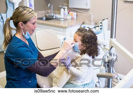 Side view of girl and dentist in dental office wearing surgical masks smiling View Large Photo Image Stock Image - Side view of girl and dentist in dental office wearing surgical masks smiling. Fotosearch