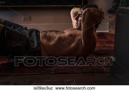 Stock Image - Side view of mature man lying on floor, hands behind head doing sit up. Fotosearch