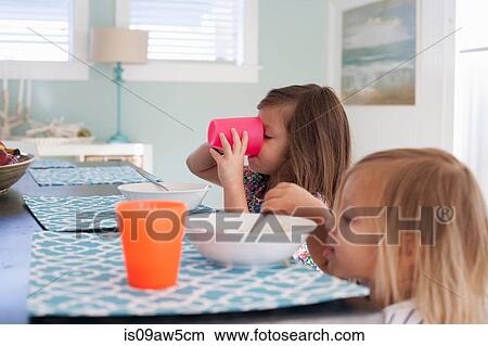 Side view of sisters at dining table eating breakfast View Large Photo Image Picture - Side view of sisters at dining table eating breakfast. Fotosearch