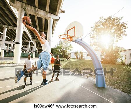 Stock Image - Side view of young man on basketball court holding basketball jumping for hoop. Fotosearch