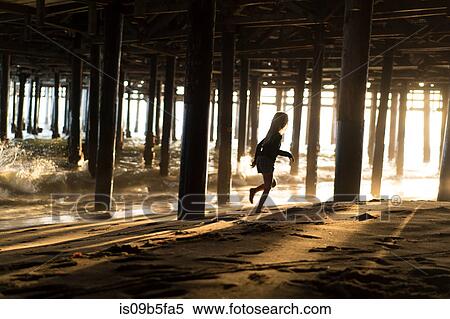 Silhouette of girl running from lapping waves underneath Santa Monica pier, California, USA View Large Photo Image Stock Photography - Silhouette of girl running from lapping waves underneath Santa Monica pier, California, USA. Fotosearch