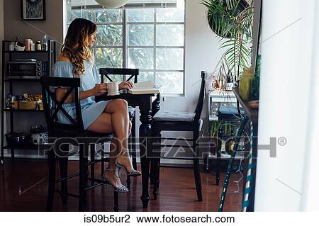 Stock Image - Sophisticated young woman reading book at table. Fotosearch