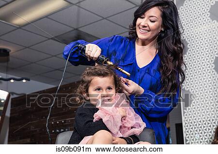 Picture - Stylist curling girl's hair in salon. Fotosearch