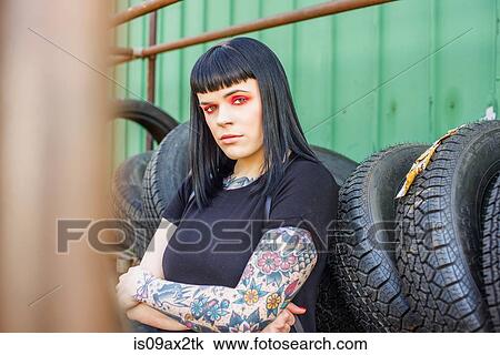 Tattooed woman leaning against tyres arms crossed looking at camera View Large Photo Image Stock Image - Tattooed woman leaning against tyres arms crossed looking at camera. Fotosearch