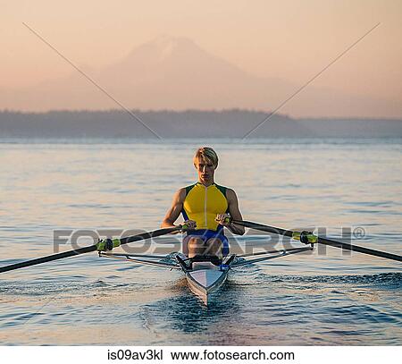 Stock Image - Teenage boy in sculling boat on water. Fotosearch