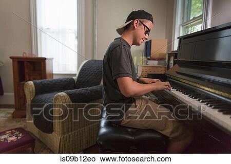 Teenage boy sitting playing piano in dining room View Large Photo Image Picture - Teenage boy sitting playing piano in dining room. Fotosearch