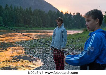 Stock Image - Teenage boys fishing in river at sunset, Washington, USA. Fotosearch