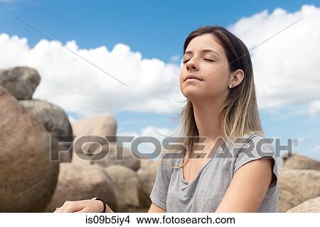 Teenage girl sitting on rocks, eyes closed, relaxing View Large Photo Image Picture - Teenage girl sitting on rocks, eyes closed, relaxing. Fotosearch