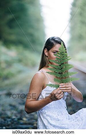 Teenage girl, sitting outdoors, holding plant in front of face View Large Photo Image Stock Photograph - Teenage girl, sitting outdoors, holding plant in front of face. Fotosearch