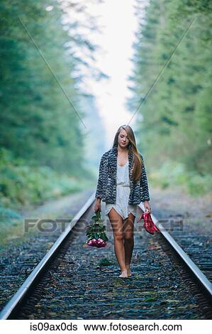 Stock Photograph - Teenage girl, walking along train track, holding red shoes and flowers. Fotosearch