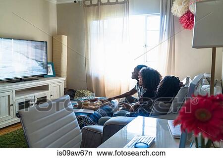 Picture - Three female friends relaxing at home, watching TV. Fotosearch