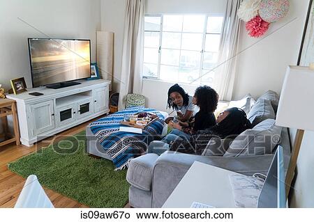 Picture - Three female friends relaxing at home, watching TV. Fotosearch