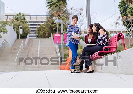 Stock Photograph - Three women outdoors, having discussion, using laptop, looking at documents. Fotosearch