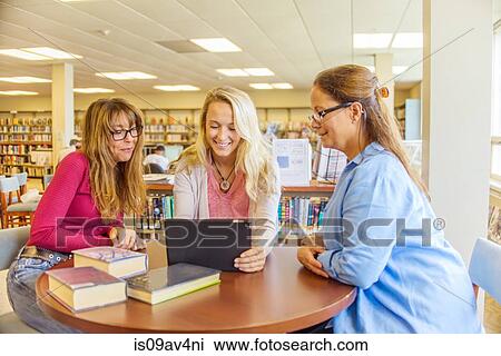 Three women using laptop at desk in library View Large Photo Image Stock Image - Three women using laptop at desk in library. Fotosearch