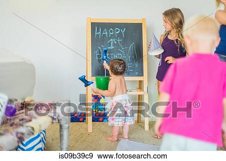 Stock Photo - Toddler playing with balloon at blackboard at birthday party. Fotosearch