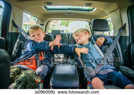 Stock Photo - Twin brothers sitting in back of vehicle, fighting. Fotosearch