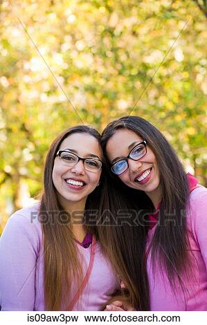 Twin sisters smiling wide in park View Large Photo Image Stock Photo - Twin sisters smiling wide in park. Fotosearch