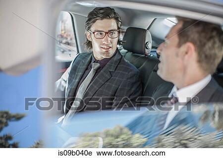 Stock Image - Two businessmen talking in car back seat. Fotosearch