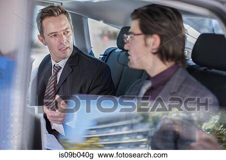 Stock Image - Two businessmen talking in car back seat. Fotosearch
